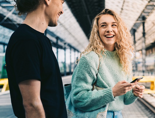 Man and woman in the railway station talking. Woman is holding a mobile phone.