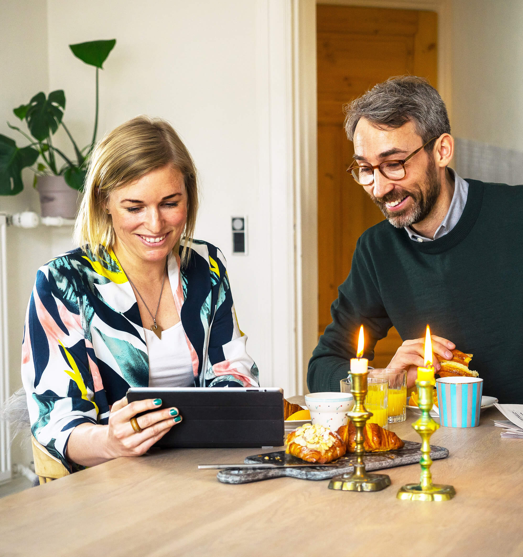 Picture of couple sitting and eating breakfast and looking at a tablet.