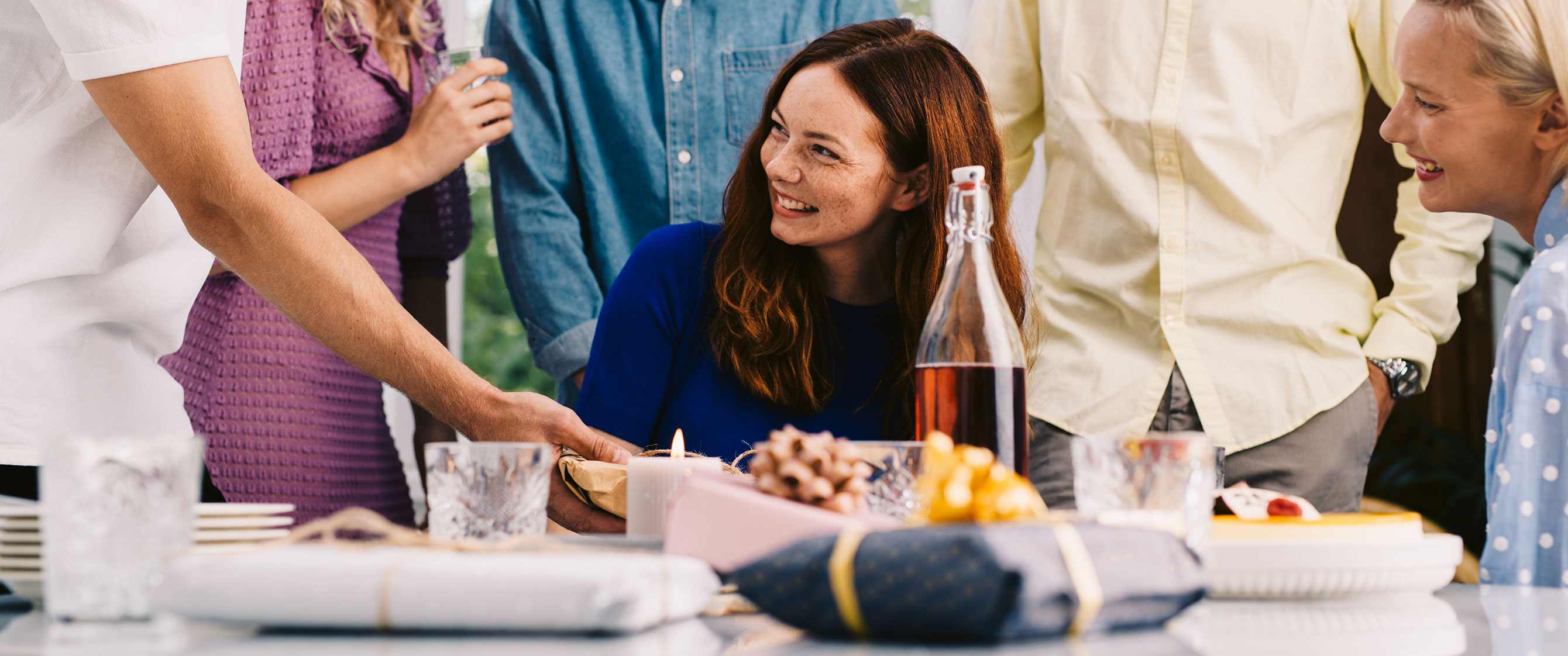 People having a joyful party. They are around a kitchen table that has gifts on it.