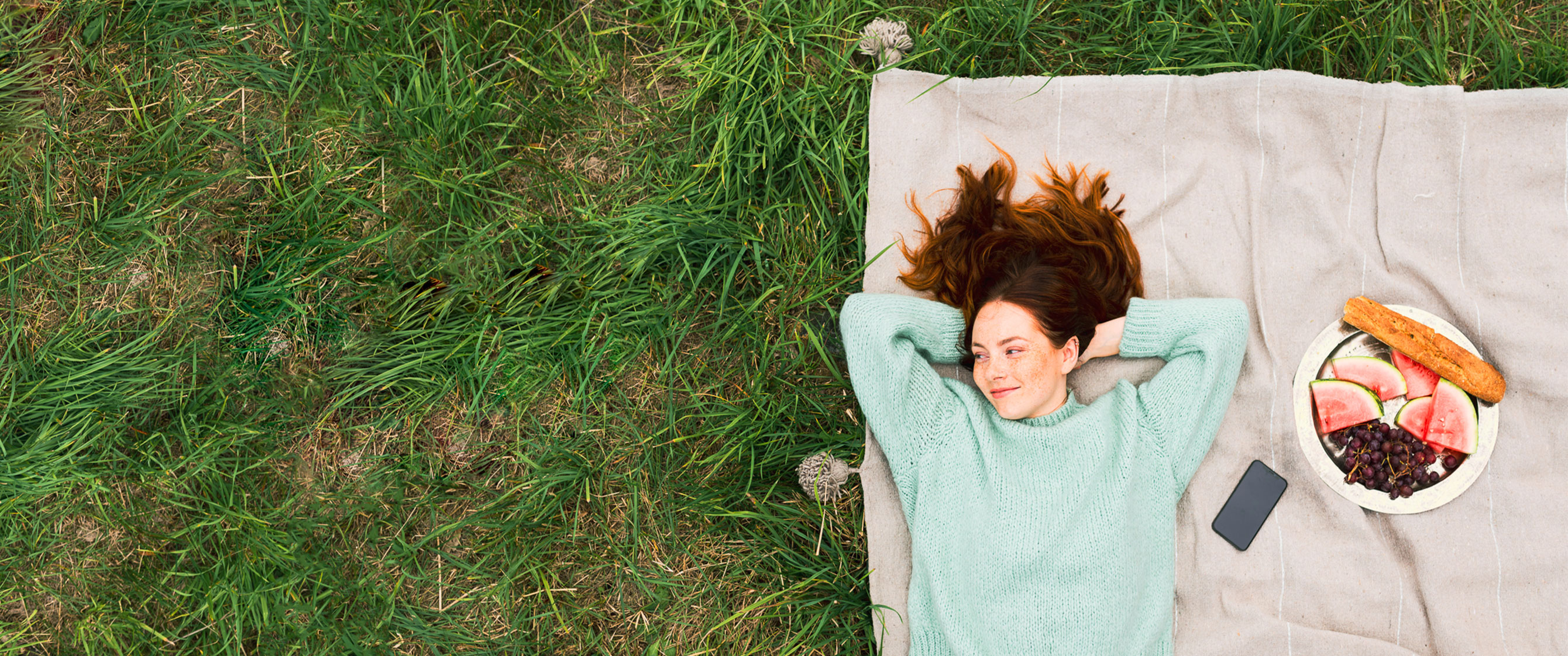 Girl in the park relaxing on a blanket which has been laid on the grass.