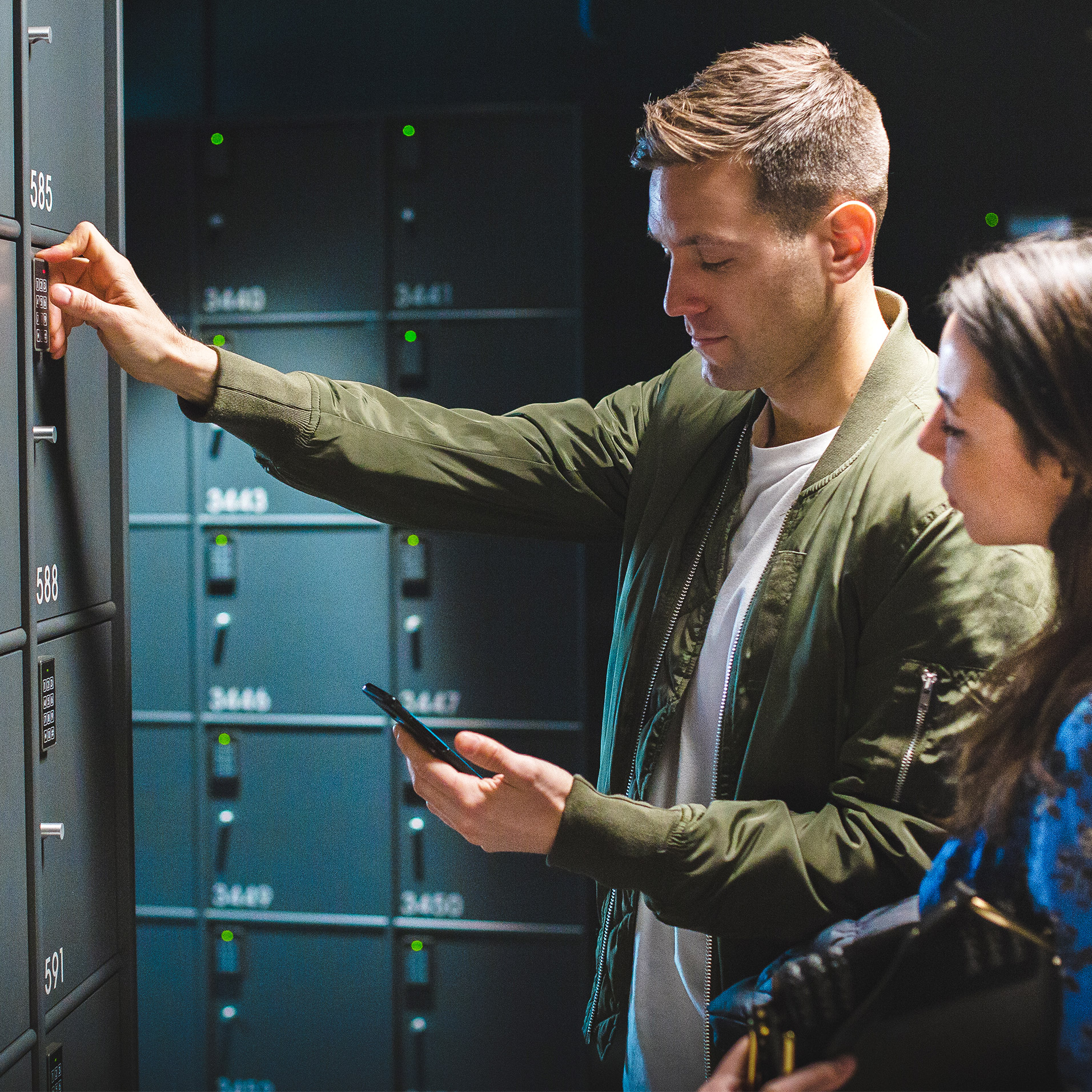Man and woman in front of lockers. Man is paying the locker fee with MobilePay.